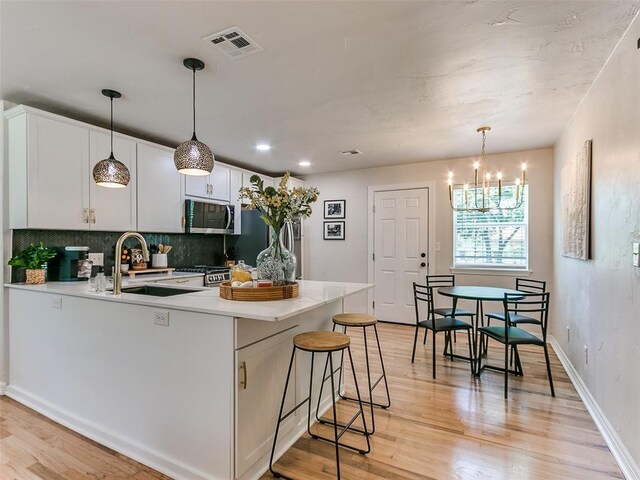 kitchen with a kitchen bar, sink, white cabinetry, decorative light fixtures, and light hardwood / wood-style floors