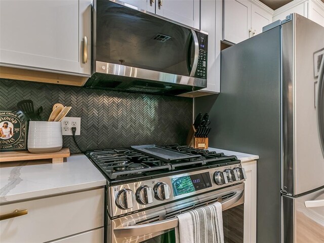 kitchen featuring white cabinetry, appliances with stainless steel finishes, backsplash, and light stone counters