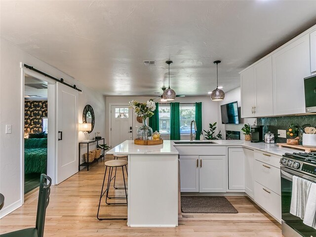 kitchen featuring sink, gas range, pendant lighting, a barn door, and white cabinets