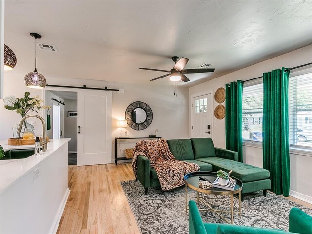 living room with sink, a barn door, ceiling fan, and light wood-type flooring