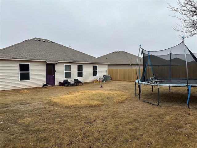 rear view of property with a trampoline and a yard