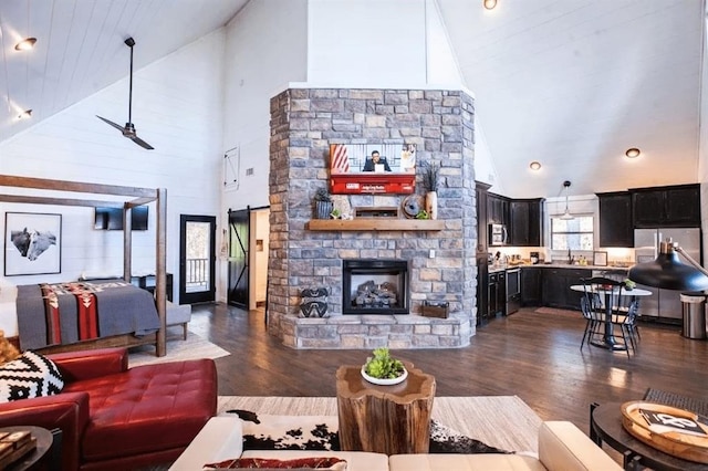 living room featuring a barn door, dark wood-type flooring, a stone fireplace, and ceiling fan