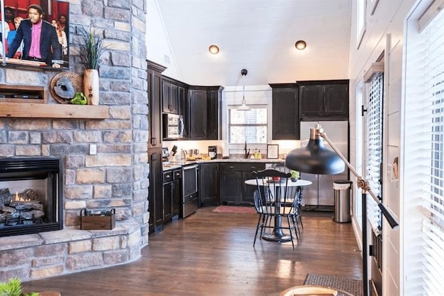 kitchen featuring vaulted ceiling, appliances with stainless steel finishes, dark hardwood / wood-style floors, a fireplace, and hanging light fixtures