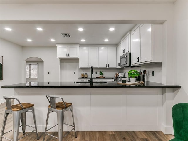 kitchen featuring a breakfast bar, white cabinetry, wood-type flooring, sink, and kitchen peninsula