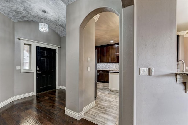 foyer with arched walkways, baseboards, and wood finished floors