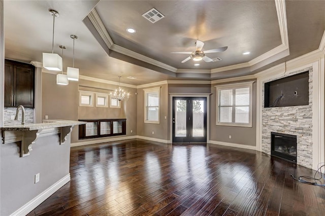 living room featuring visible vents, a fireplace, a tray ceiling, and dark wood finished floors