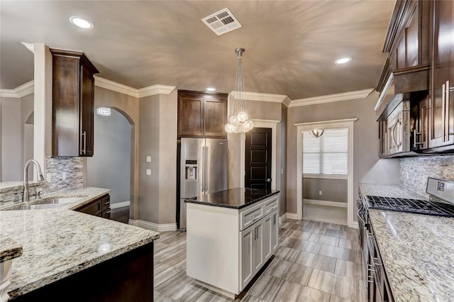 kitchen featuring visible vents, appliances with stainless steel finishes, dark stone countertops, decorative light fixtures, and a sink