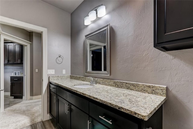 bathroom featuring a textured wall, vanity, baseboards, and wood finished floors