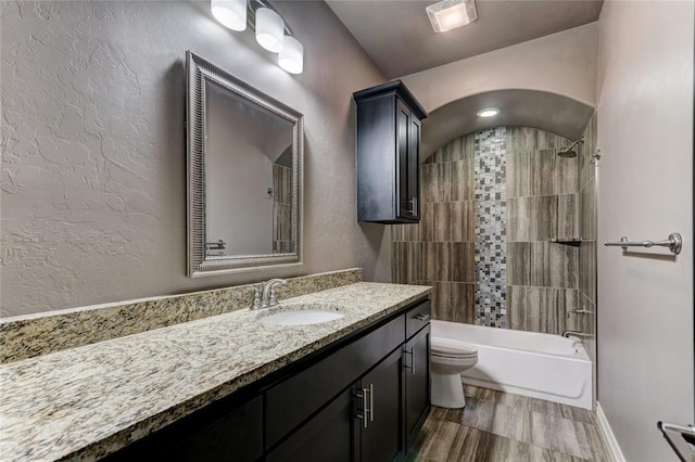 full bathroom with a textured wall, toilet, wood finished floors, vanity, and shower / washtub combination