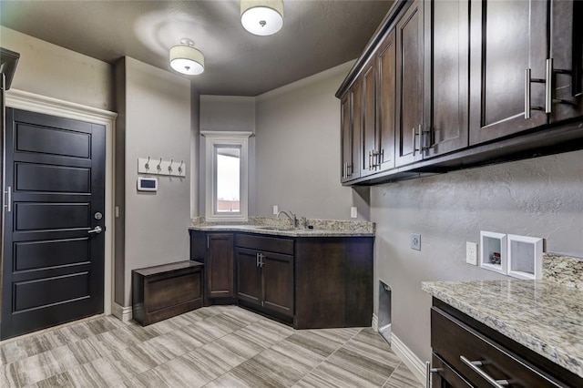 kitchen featuring dark brown cabinetry, baseboards, light stone counters, and a sink