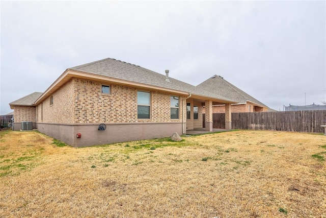 back of property with a lawn, roof with shingles, fence, central AC, and brick siding