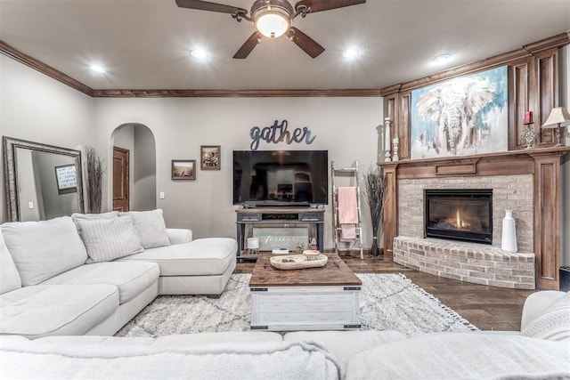 living room featuring hardwood / wood-style flooring, ornamental molding, ceiling fan, and a fireplace