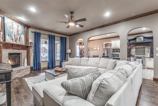 living room with dark hardwood / wood-style flooring, a brick fireplace, ornamental molding, and ceiling fan