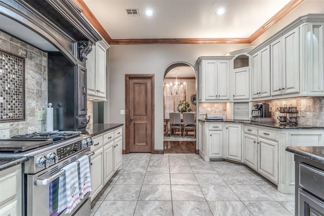 kitchen with white cabinetry, high end range, a chandelier, dark stone countertops, and ornamental molding