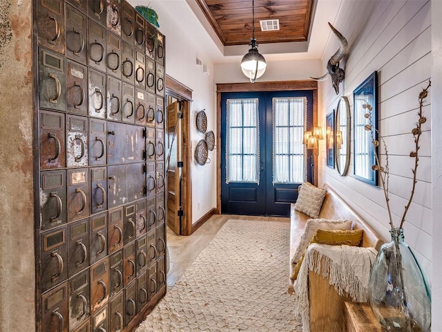 entrance foyer featuring a tray ceiling, crown molding, wooden ceiling, light wood-type flooring, and french doors