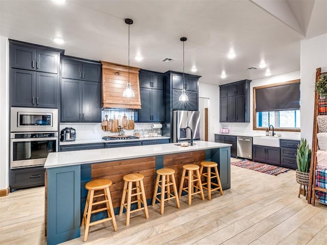 kitchen featuring stainless steel appliances, pendant lighting, a kitchen island with sink, and a breakfast bar area