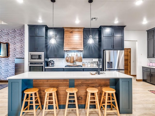 kitchen with decorative light fixtures, a breakfast bar area, stainless steel appliances, and a center island with sink