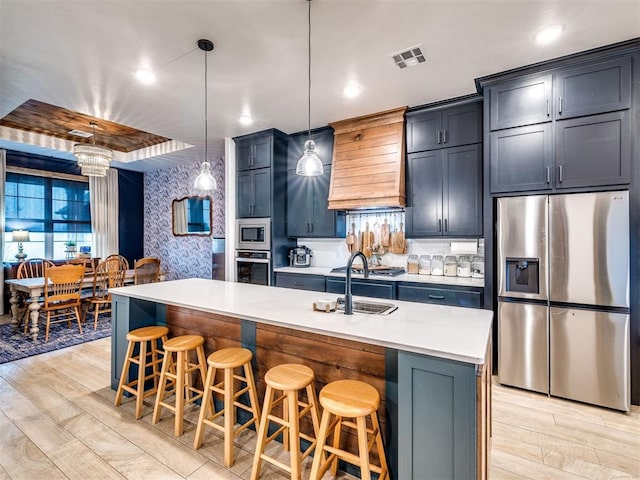 kitchen with a breakfast bar, stainless steel appliances, custom range hood, a center island with sink, and decorative light fixtures