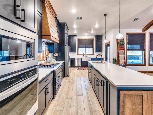 kitchen featuring sink, light hardwood / wood-style flooring, hanging light fixtures, stainless steel appliances, and a center island with sink