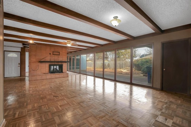 unfurnished living room featuring parquet flooring, ceiling fan, a brick fireplace, a textured ceiling, and beam ceiling