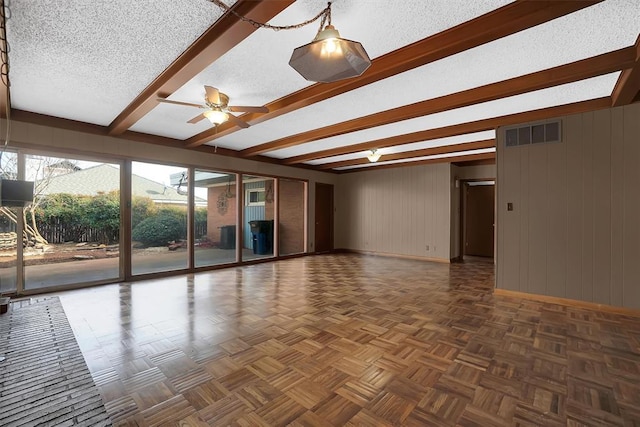 spare room featuring dark parquet flooring, a textured ceiling, wooden walls, beamed ceiling, and ceiling fan