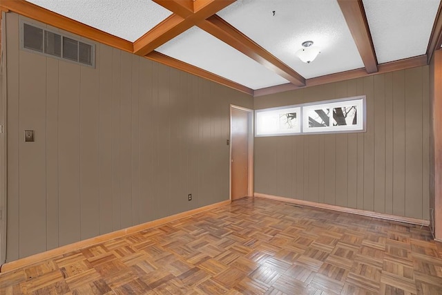 spare room featuring a textured ceiling, light parquet flooring, and beamed ceiling