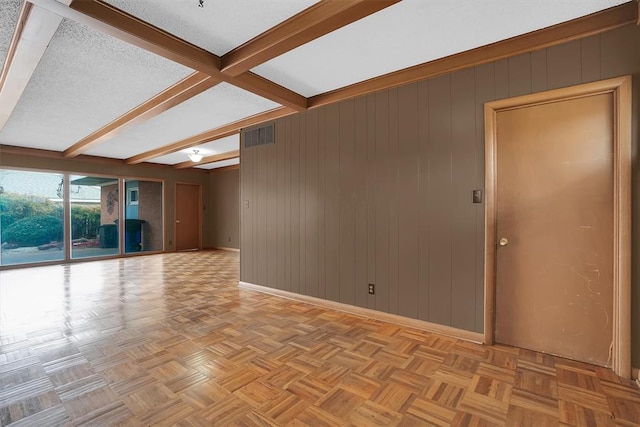 empty room featuring light parquet floors, a textured ceiling, and beam ceiling