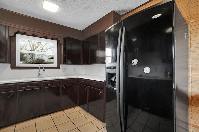 kitchen with sink, light tile patterned floors, dark brown cabinetry, black fridge, and a textured ceiling