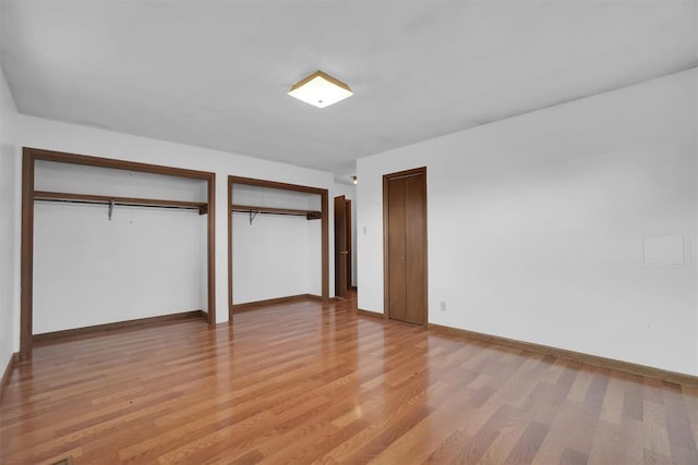 unfurnished bedroom featuring two closets and light wood-type flooring