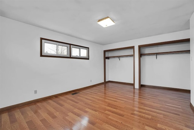 unfurnished bedroom featuring two closets and light hardwood / wood-style floors