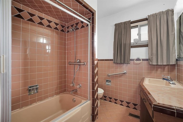 full bathroom with tile walls, tile patterned flooring, tiled shower / bath combo, vanity, and toilet