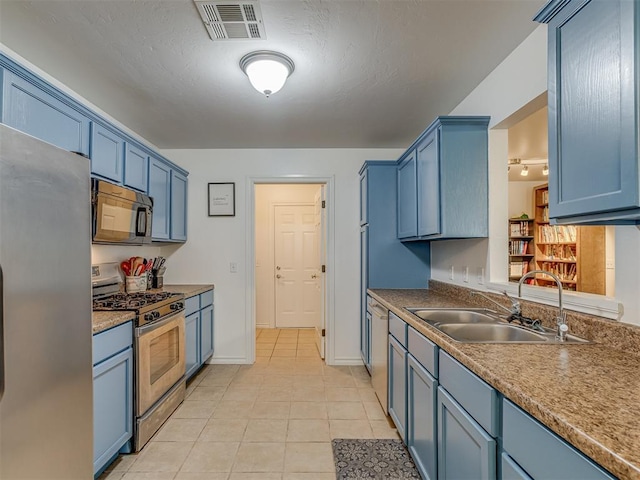 kitchen with appliances with stainless steel finishes, sink, light tile patterned floors, and blue cabinetry