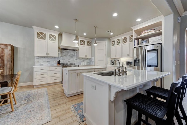 kitchen featuring sink, custom exhaust hood, stainless steel fridge, an island with sink, and white cabinets