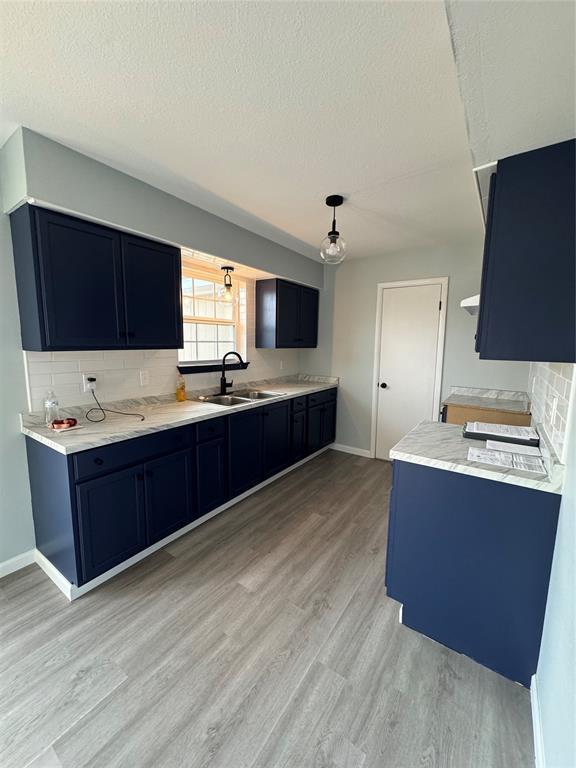 kitchen featuring blue cabinets, sink, light wood-type flooring, backsplash, and a textured ceiling