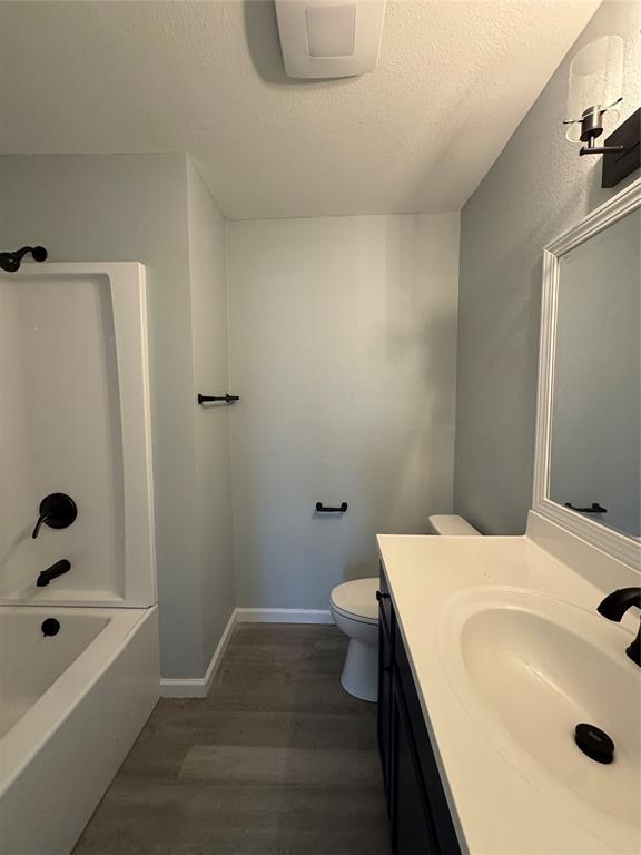 full bathroom featuring wood-type flooring, vanity, toilet, tub / shower combination, and a textured ceiling