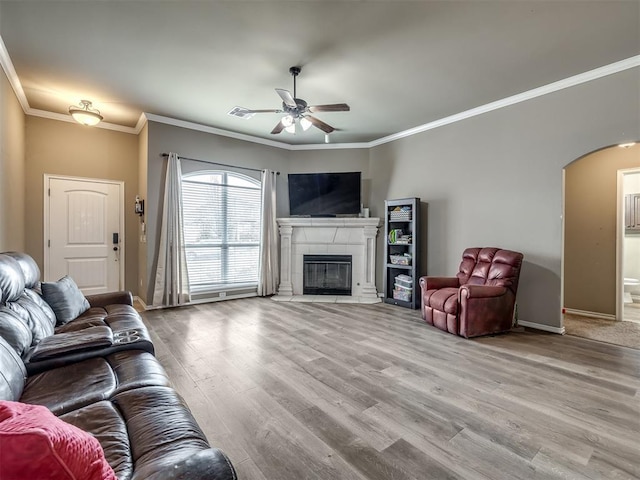 living room featuring a tiled fireplace, hardwood / wood-style floors, crown molding, and ceiling fan