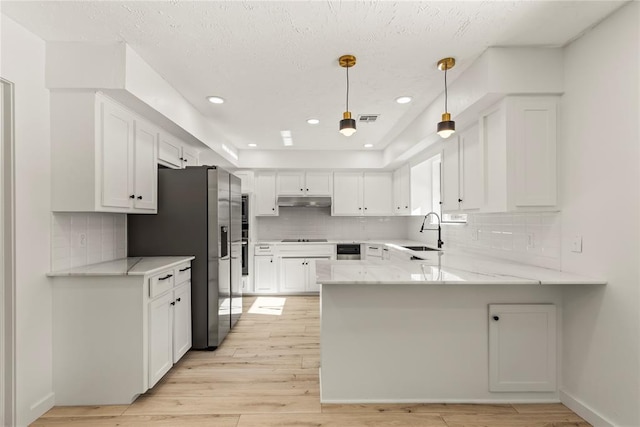 kitchen with sink, kitchen peninsula, white cabinets, and decorative light fixtures