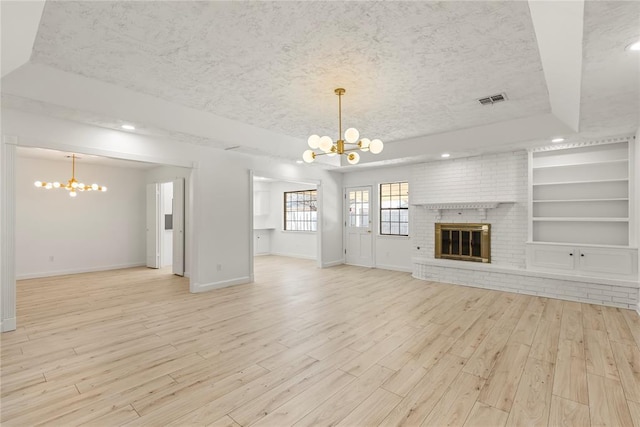 unfurnished living room featuring a textured ceiling, built in shelves, a raised ceiling, and a chandelier