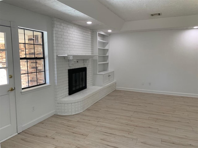 unfurnished living room featuring built in shelves, a fireplace, light hardwood / wood-style floors, and a textured ceiling