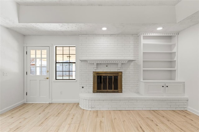 unfurnished living room featuring built in shelves, a fireplace, and light wood-type flooring