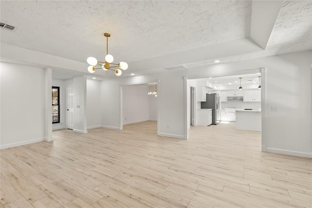 unfurnished living room featuring an inviting chandelier, a tray ceiling, a textured ceiling, and light hardwood / wood-style flooring