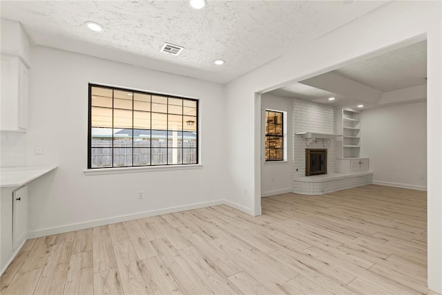 unfurnished living room featuring built in shelves, a fireplace, a textured ceiling, and light wood-type flooring