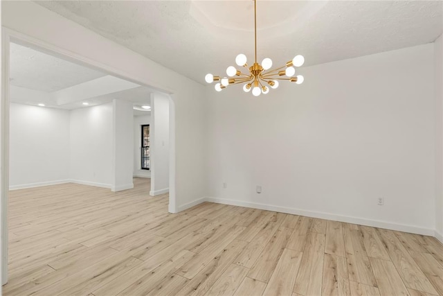 empty room featuring a textured ceiling, an inviting chandelier, and light hardwood / wood-style flooring