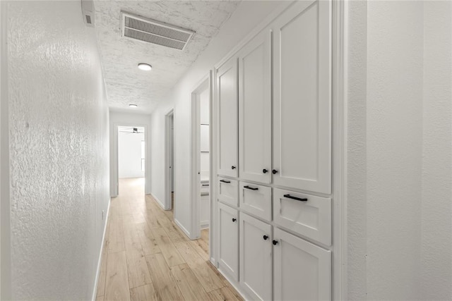 hall with light hardwood / wood-style floors and a textured ceiling