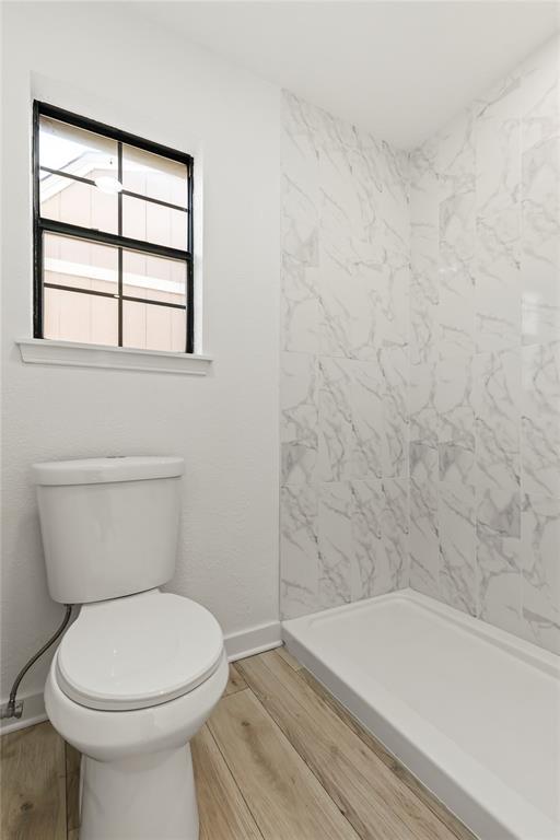 bathroom with tiled shower, wood-type flooring, and toilet