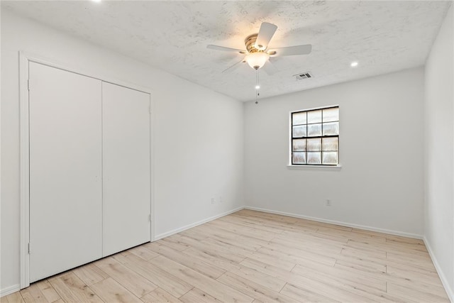 unfurnished bedroom featuring ceiling fan, a textured ceiling, light hardwood / wood-style floors, and a closet