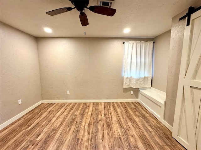 spare room featuring ceiling fan, a barn door, and hardwood / wood-style floors