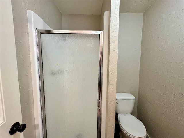 bathroom featuring a shower with door and toilet