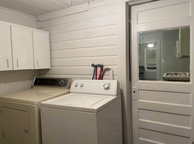 laundry area with cabinets, washing machine and dryer, and wood walls