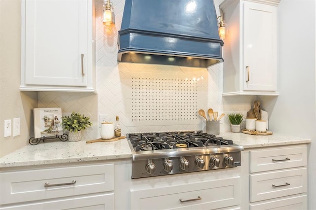 kitchen with backsplash, light stone countertops, white cabinets, custom exhaust hood, and stainless steel gas stovetop